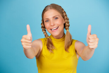 Portrait of positive smiling girl dressed in yellow t-shirt showing thumbs up over blue background