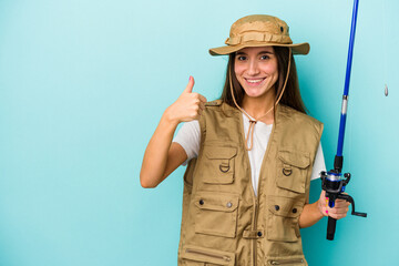Young caucasian fisherwoman isolated on blue background smiling and raising thumb up