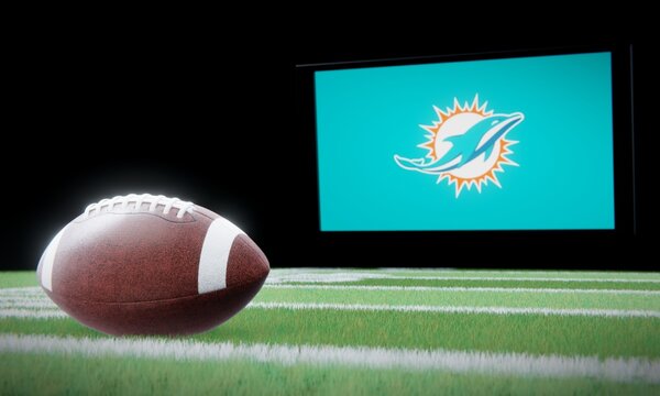 American football in foreground with logo of NFL team Miami Dolphins projected on screen in background. Editorial 3D illustration