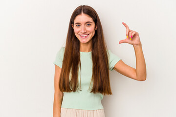 Young caucasian woman isolated on white background holding something little with forefingers, smiling and confident.