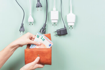 Woman's hand takes euro money banknotes from wallet near many power cable cords with Eu plugs...