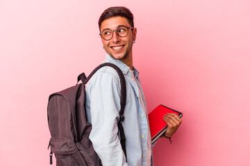 Young caucasian student man holding books isolated on pink background  looks aside smiling,...