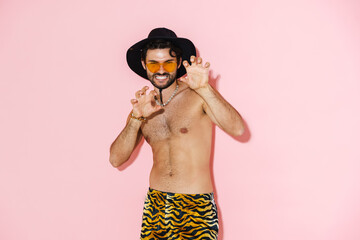 Young shirtless man wearing shorts grimacing and gesturing at camera - obrazy, fototapety, plakaty
