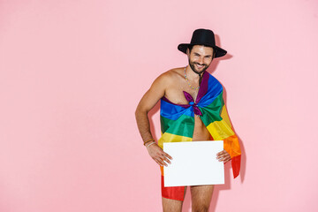 Young shirtless man with rainbow flag smiling while showing placard