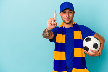 Young soccer fan man holding a ball isolated on blue background  showing number one with finger.