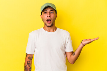 Young caucasian man with tattoos isolated on yellow background  impressed holding copy space on palm.