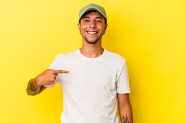 Young caucasian man with tattoos isolated on yellow background  person pointing by hand to a shirt copy space, proud and confident