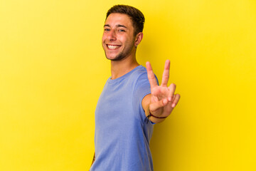 Young caucasian man with tattoos isolated on yellow background  showing victory sign and smiling broadly.