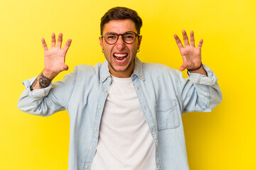 Young caucasian man with tattoos isolated on yellow background  showing claws imitating a cat,...
