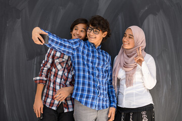 Group of arab teens taking selfie photo on smart phone with black chalkboard in background. Selective focus 