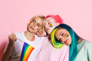 Young three women hugging while posing with rainbow flag