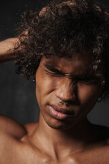 Shirtless black man with piercing holding his head and frowning