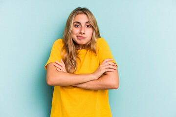 Young caucasian blonde woman isolated on blue background  shrugs shoulders and open eyes confused.