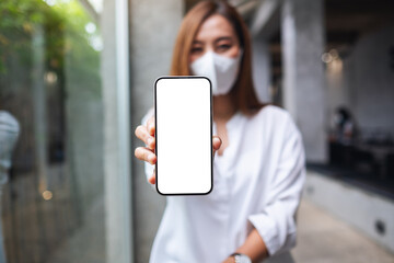 Mockup image of a woman wearing protective face mask, showing mobile phone with blank white screen for Covid-19 concept