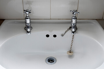 White porcelain bathroom sink with 2 silver taps and plug on chain