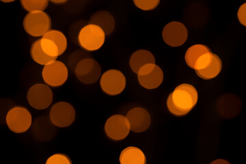 Defocused bokeh lights on black background, an abstract naturally blurred backdrop for Christmas eve or birthday party. Festive light texture. Yellow and red garland in blur. Overlay effect for design