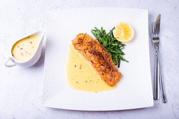 Salmon with beurre blanc sauce, spinach and lemon. Garnished with leeks. Traditional French dish. Close-up.