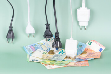 Many power cable cords with Eu plugs hanging over pile of Euro money coins and bills. Energy...