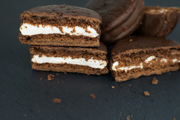Cookies in chocolate glaze and white cream filling scattered on a dark background.