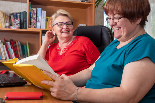 Two Women Are Sitting At Table, Laughing And Looking At Book. Generation Of Baby Boomers. Selective Focus.