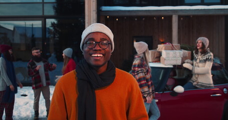 Happy smiling young African American man in winter hat, eyeglasses smiling at camera at fun Christmas party slow motion.