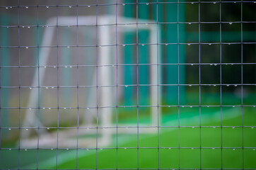 Blurred soccer goal behind a fence mesh with raindrops