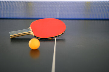 Red racquet with orange table tennis ball put on the table with blue net for ready to play ping pong.