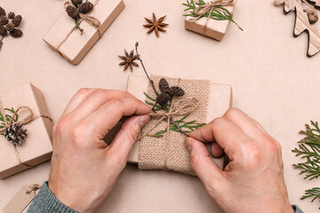 Festive decoration of gifts in eco-style,male hands close-up,top view.Gift boxes are wrapped in craft paper,decorated with thuja leaves and cones.Christmas,New Year and eco-friendly concept.