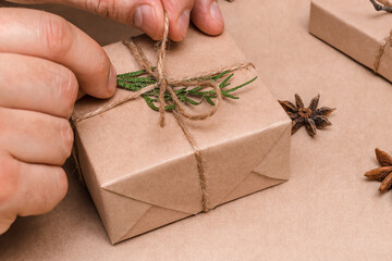 Cristmas decoration of gifts in eco-style,male hands close-up.Gift boxes are wrapped in craft paper,decorated with thuja leaves.Christmas,New Year and eco-friendly concept.