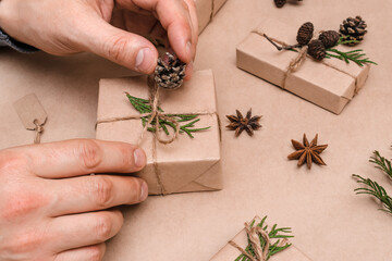 Cristmas decoration of gifts in eco-style,male hands close-up.Gift boxes are wrapped in craft paper,decorated with thuja leaves and cones.Christmas,New Year and eco-friendly concept.