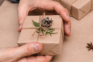 Cristmas decoration of gifts in eco-style,male hands close-up.Gift boxes are wrapped in craft paper,decorated with thuja leaves and cones.Christmas,New Year and eco-friendly concept.