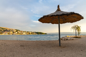 empty gravel beach in Croatia with a thatched reed sun umbrella and golden evening light on the Adriatic coast