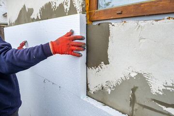Construction worker installing styrofoam insulation sheets on house facade wall for thermal protection - obrazy, fototapety, plakaty