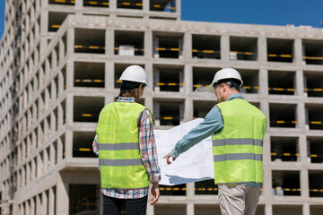 two engineers, a man and a woman in white helmets and protective vests, work at the construction site. European engineers or fire safety specialists at the construction site. handshake of partner