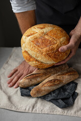 an adult European male baker holds a round fresh bread in his hands. a man in a bakery holds a yeast-free bread on sourdough and a baguette. cool and healthy bread for the whole family. vegan food for
