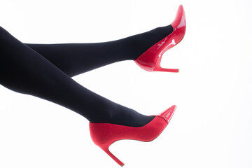 Feet of a girl in pantyhose with red shoes on a white background