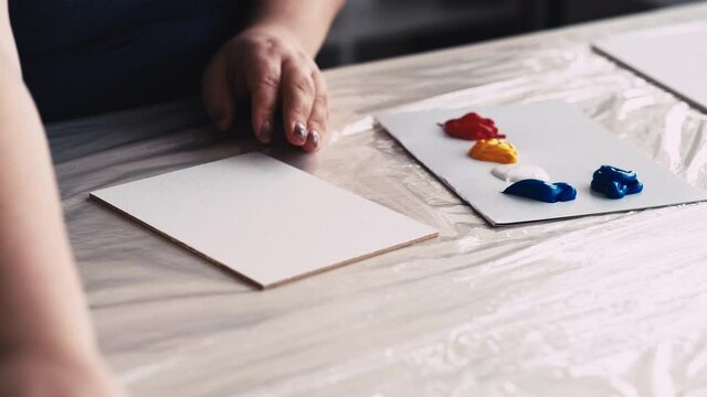Painting preparation. Artistic tools. Creative process. Unrecognizable woman putting colorful paints palette board and spatula on table light room.