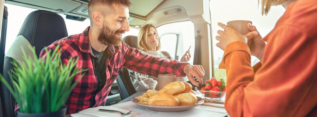 Happy friends having breakfast in a camper van in the morning