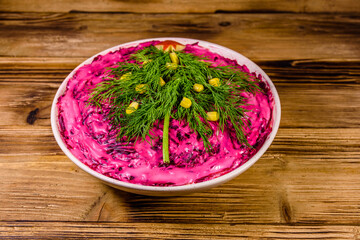 Ceramic plate with russian traditional new year salad herring under fur coat (shuba) decorated with christmas tree made from dill on rustic wooden table