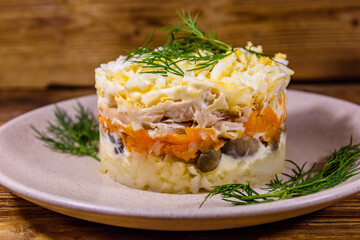 Salad with chicken breast, marinated mushrooms, carrot, eggs, boiled potato and mayonnaise on a wooden table