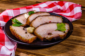 Slices of baked pork belly, garlic and parsley on a black plate