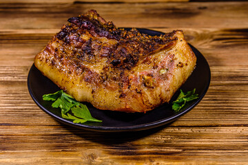 Baked piece of pork belly and parsley on a black plate