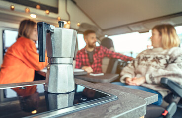 Italian coffee maker with group of people talking in the background in a camper van. Selective focus on coffee maker in the foreground