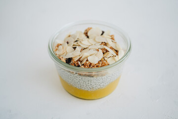 Mango chia pudding with granola and almond flakes on white table