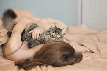 Young woman in bed at home with tabby cat