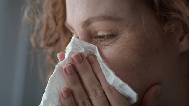 Close up of young caucasian  red head woman sneezing and blowing nose into tissue at home. Shot with RED helium camera in 8K.   