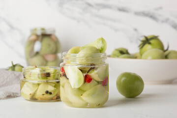 Green tomatoes for canning in a glass jar on a light background. Unripe tomatoes for harvest.