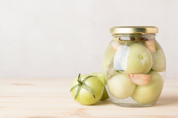 Obraz na płótnie Canvas Green tomatoes for canning in a glass jar on a light wooden background. Unripe tomatoes for harvest.