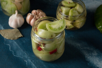 Green tomatoes for canning in a glass jar on a blue marble background. Unripe tomatoes for harvest.