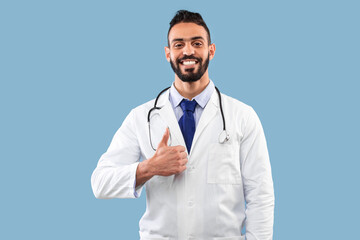 Happy Middle Eastern Doctor Man Gesturing Thumbs-Up Posing Over Blue Background